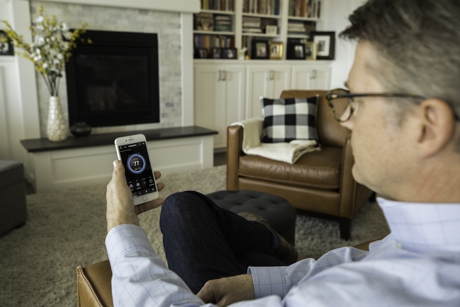  A man sitting in his living room looking at his smart come control app on his smartphone.